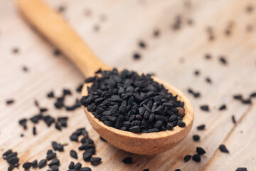 Black cumin seeds on wooden spoon on wooden background
