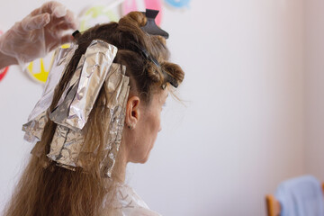 Hairdresser with plastic gloves applies aluminum foil to blonde woman for streaks. Hair stylist...
