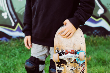 Close up of an skater boy with an old skateboard in front of a graffiti mural