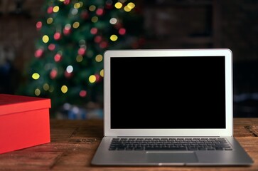 Blank screen laptop on table with Christmas decorations and Christmas lights in the background. Online shopping concept.