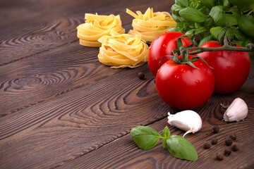 Raw tagliatelle pasta with fresh basil, garlic and branch of tomatoes on rustic wooden table