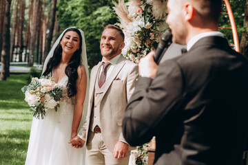 The host at the wedding interviews the bride and groom. Newlyweds on the background of a floral arch.
