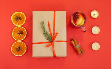 Flat lay on a red background with a Christmas present, a cup of mulled wine with ingredients and candles. Horizontal orientation, selective focus, top view.