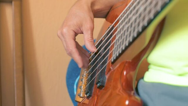 The musician plays a six-string bass guitar in his home Studio. Close up. Soft focus