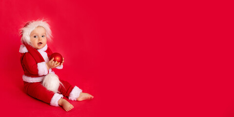 a child in a Santa Claus costume on a red background, banner, space for text