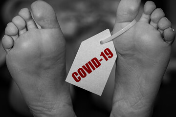 close up feets of corpse in morgue on table tagged with the inscription COVID-19. Pandemic,...