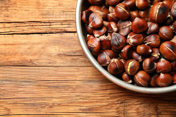 Delicious roasted edible chestnuts on wooden table, top view. Space for text