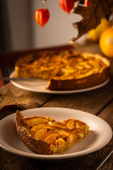 Apple pie with caramel on a wooden background, autumn bouquet in a vase, portion of pie in a plate close-up , autumn bouquet in a vase