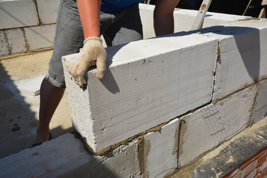 A building contractor is building a wall lying autoclaved aerated concrete (AAC) blocks over brick foundation with bitumen asphalt waterproofing membrane installed.