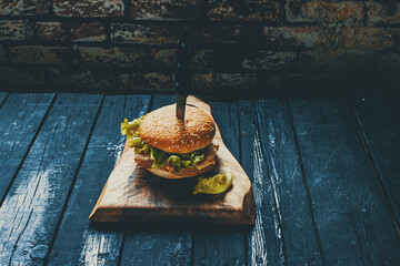 Homemade burger with ham, cheese, salad and pomegranate, pierced by a knife on a wooden board
