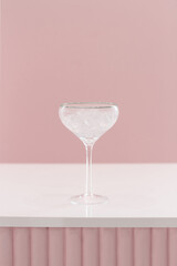 Cocktail glass wineglass with silver golden border on a bar counter on a white pink background