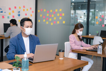 Asian workers in offices wear face masks to prevent the spread of COVID-19. Working in the new normal era and Social distance.