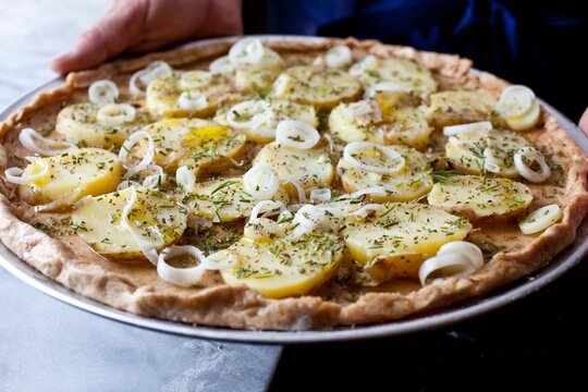 Person holding tray with pizza with green garlic, potatoes and herbs