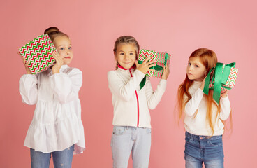 Giving and getting presents on Christmas holidays. Group of happy smiling children having fun, celebrating isolated on pink studio background. New Year 2021 meeting, childhood, happiness, emotions.