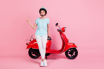 Obraz na płótnie Canvas Full size photo of cheerful nice girl stand moped point empty space wear trousers footwear slam t-shirt isolated on pink background