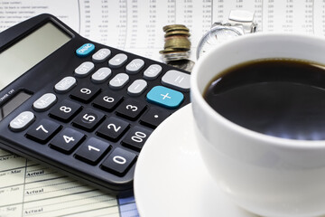 a black calculator along with a stack of pennies on financial documents and a blurry Cup of coffee. Business concept.