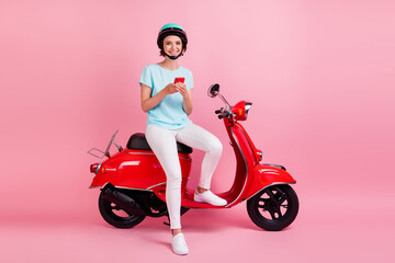 Fototapeta na wymiar Photo of cheerful pretty young woman sit moped sms telephone dress white trousers sneakers blue slam t-shirt isolated on pink background