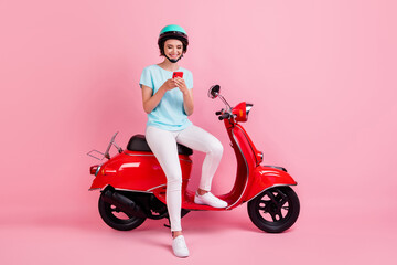 Fototapeta na wymiar Photo of cheerful pretty girl sit moped chatting telephone wear white trousers sneakers blue slam t-shirt isolated on pink background