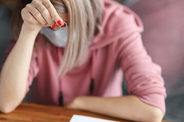 Woman in medical protective mask sits with her head down and holds wedding ring. Increase in divorces after quarantine concept