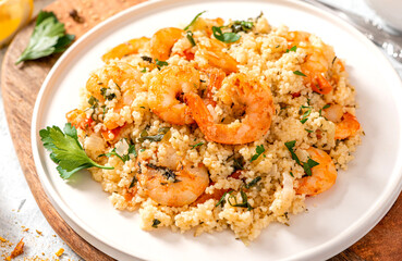 Couscous with shrimps, tomatoes, onions, and herbs in a white bowl close-up. Tasty Moroccan food with couscous and seafood.
