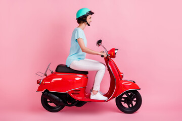 Fototapeta na wymiar Profile view portrait of pretty glad girl riding red moped wear slam t-shirt trousers shoes isolated on pink color background