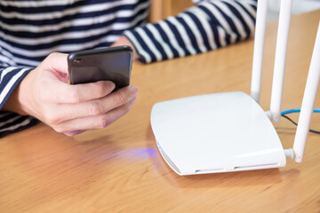 Selective focus at internet router with man using smart phone device to connect to internet or wireless connection at home, High speed broadband network concept.