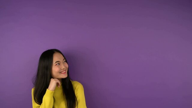 puzzled young asian woman in bright yellow sweater looks right. Free space for text and speech bubble. isolated purple background. 4K