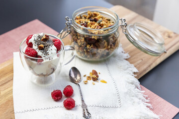 Granola in a jar and in a cup with yogurt and raspberry on the table. Granola is a breakfast food and snack food consisting of rolled oats, nuts, honey, that is baked until golden brown