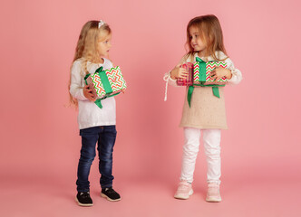 Giving and getting presents on Christmas holidays. Two little smiling children having fun, celebrating isolated on pink studio background. New Year 2021 meeting, childhood, happiness, emotions.