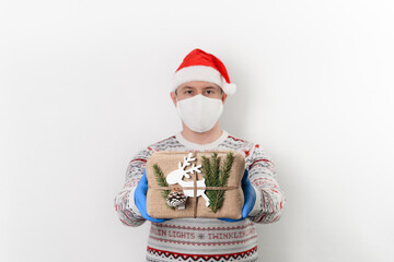 Delivery man holding gift box in eco-friendly reusable packaging on white background. He wearing protection mask and medical rubber gloves safety form coronavirus. Safe christmas delivery