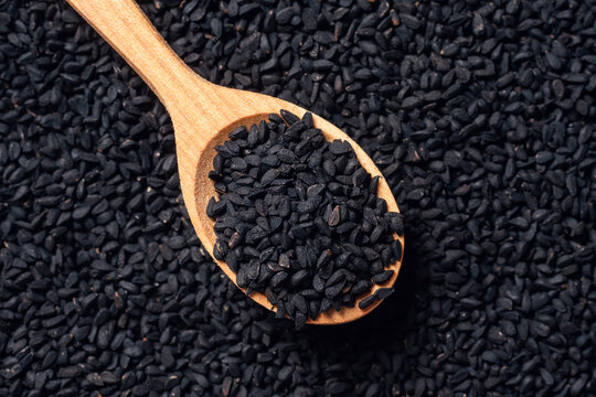 Black cumin seeds on wooden spoon on wooden background