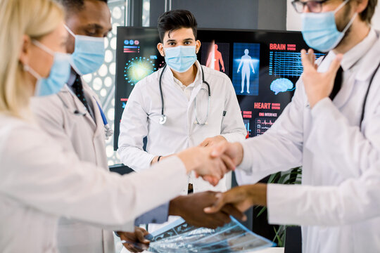 Pandemy, outbreak of coronavirus concept. Close up cropped image of multiethnic group of doctors with face masks, shaking hands on the morning staff meeting. Focus on Indian doctor standing behind