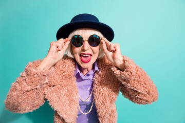 Photo of surprised senior lady wear retro jacket headwear arms eyeglasses isolated teal color...