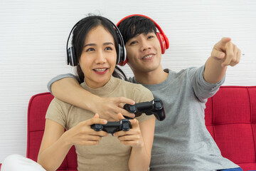 Couples play games and listen to sound through bluetooth headphones and sitting on sofa at the...