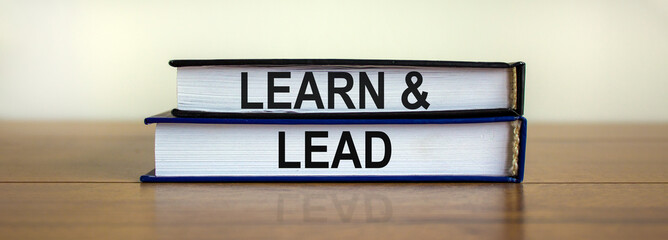 Books with the text 'learn and lead' on beautiful wooden table, white background. Business concept, copy space.