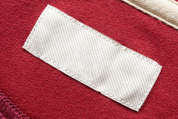 Blank white laundry care clothes label on red fabric texture background