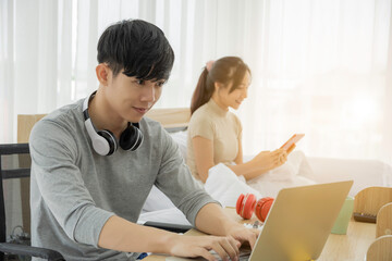 A good looking asian man work on his desk. young man was successful career. His job is sell online, with a girlfriend sitting in bed assistant to work