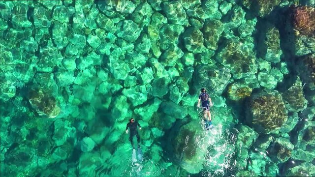 erial top shot of two people snorkeling in blue transparent water.