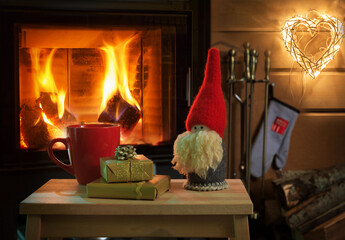 Mug of hot chocolate or coffee, gifts and Christmas gnome on vintage wood table in front of Fireplace as a background.