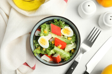 Delicious salad with crab sticks and eggs in bowl on white wooden table, flat lay
