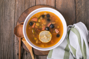 Slavic Solyanka soup in a white bowl on dark wooden background with copy space. Top view. Famous traditional Ukrainian and Russian saltwort soup with lemon.
