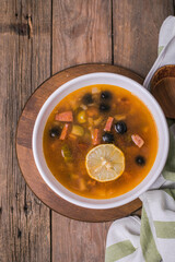 Slavic Solyanka soup in a white bowl on dark wooden background with copy space. Top view. Famous traditional Ukrainian and Russian saltwort soup with lemon.
