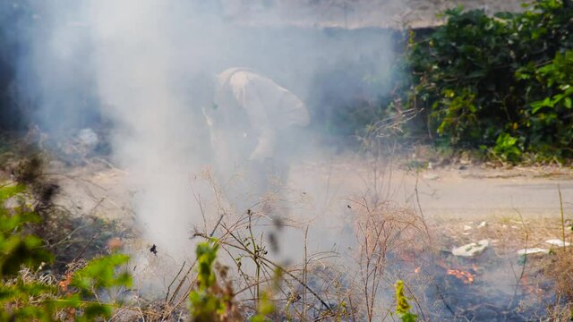 man hidden from view by thick black white sooty smoke shovelling thrash into fire to burn crops and garbage causing more air pollution as the winters start in Delhi NCR. Shows the daily activities tha