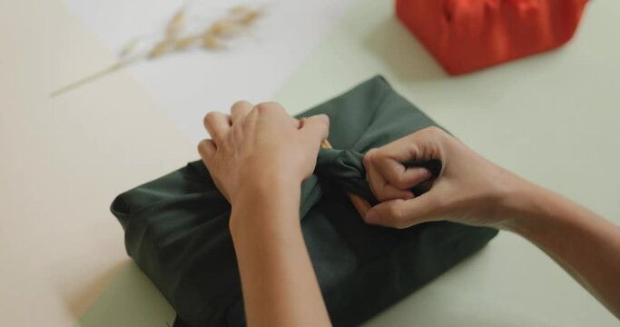 Female hands wrapping a gift in green tissue and tying it with a cinnamon, minimalism concept, 4k