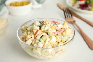 Delicious salad with crab sticks in glass bowl on white table