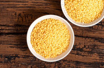 Dry ptitim close-up. Toasted pasta ptitim (petit plomb or Israeli couscous) in a bowl on a wooden background top view.  Copy space.