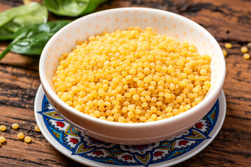 Dry ptitim close-up. Toasted pasta ptitim (petit plomb or Israeli couscous) in a bowl on a wooden background.
