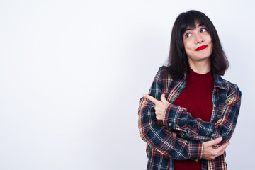 Portrait of Beautiful young Caucasian woman standing against white background posing on camera with tricky look, presenting product with index finger. Advertisement concept.