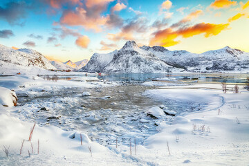 Gorgeous frozen Flakstadpollen and Boosen fjords with cracks on ice during sunrise with Hustinden mountain on background on Flakstadoya island