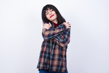 Beautiful young Caucasian woman standing against white background. Hugging oneself happy and positive, smiling confident. Self love and self care.